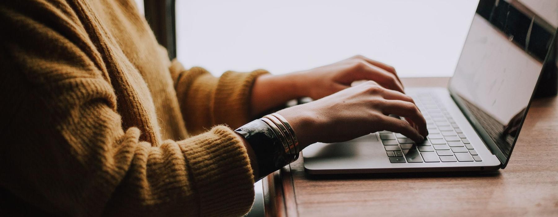 woman types on her laptop near large window